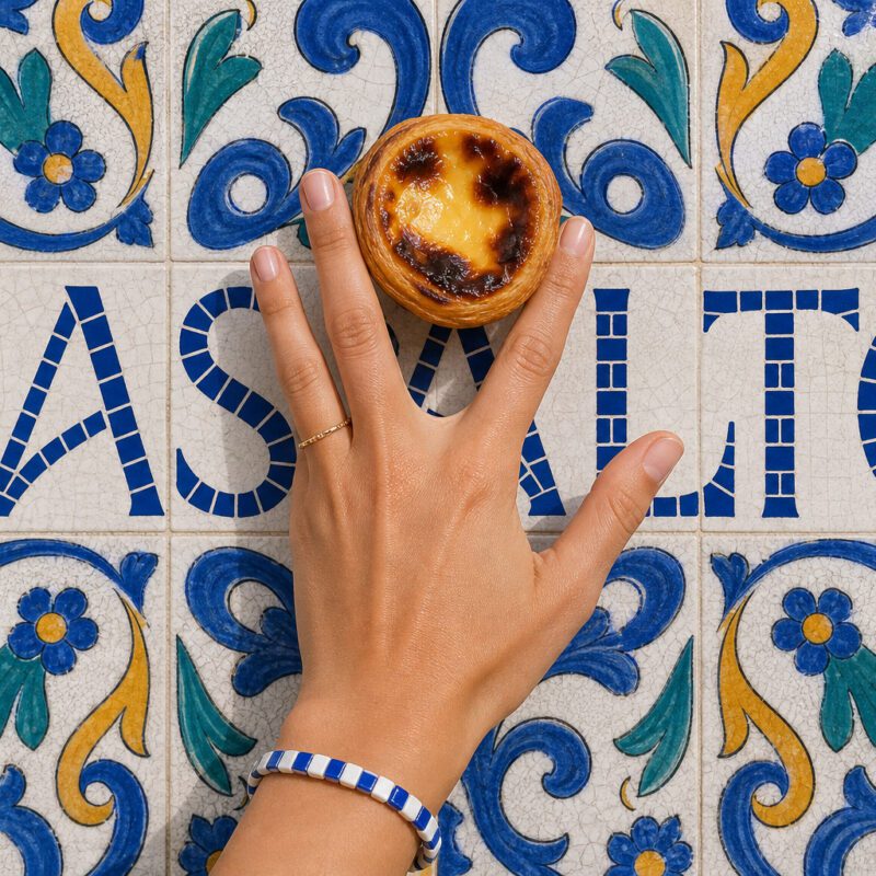Mão com pastel de nata sobre azulejo com o nome Basalto